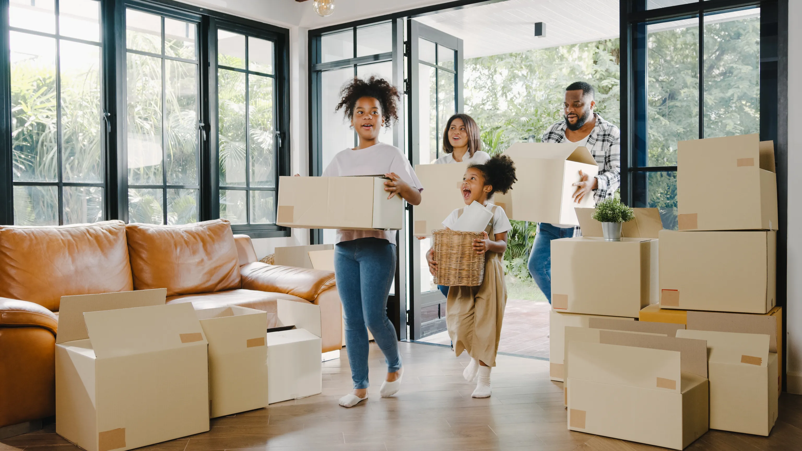 A smiling family carrying moving boxes through the front door of their new home, sunlight streaming in behind them.